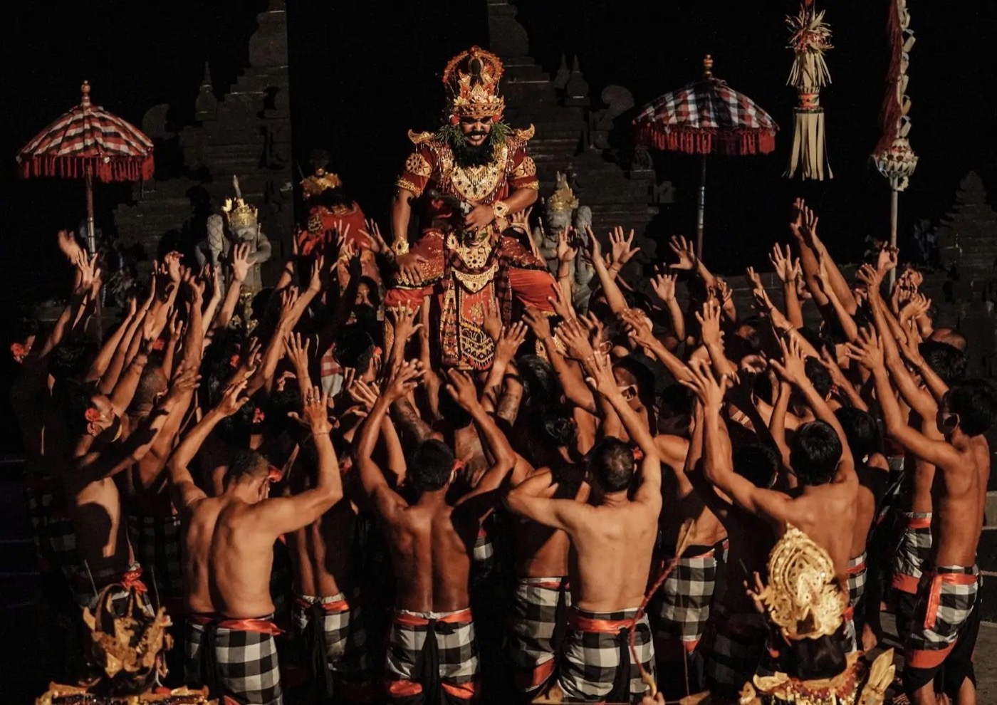 Kecak performers reaching towards a central figure at night